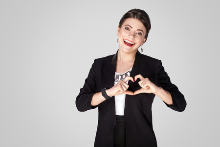 Love concept. Creative woman showing heart shape sign. Studio shot, indoor. Isolated on grey backgroundの写真素材