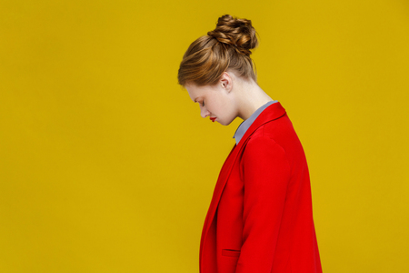 Profile worry redhead woman in red jacket nervous. Studio shot, isolated on yellow backgroundの写真素材