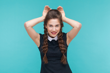 Funny young woman showing rabbit sign and smile. Indoor, studio shot on blue backgroundの写真素材