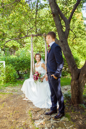 attractive wife sitting on swing and looking at husband at summer gardenの写真素材