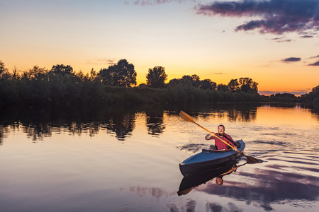sporty man kayaking on river surrounded by forest at sunsetの写真素材