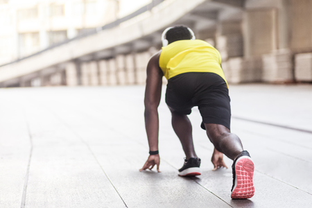 Spine view. African athlete in running start pose. Outdoor shot, morning. Spring or summer