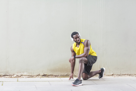 African runner in yellow sportswear stretching before doing morning workout looking at camera nd toothy smiling. Outdoor shot, morning. Spring or summerの写真素材