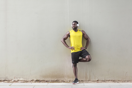 Sporty afro man standing near old wall, doing morning gymnastics. Outdoor shot, morning. Spring or summerの写真素材