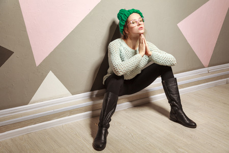 attractive woman wearing glasses and warm dotted pullover clothes and green hat posing near pastel wall. indoor, studio shot.の写真素材