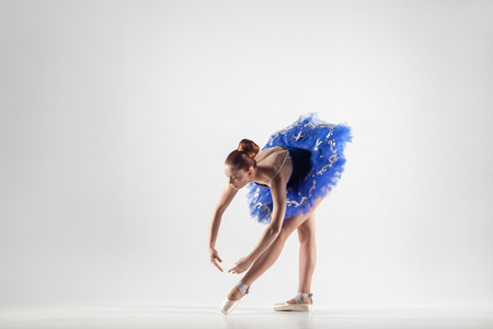 Young beautiful ballerina with bun collected hair wearing blue dress and pointe shoes dancing gracefully isolated on white background. indoor, studio shot.の写真素材