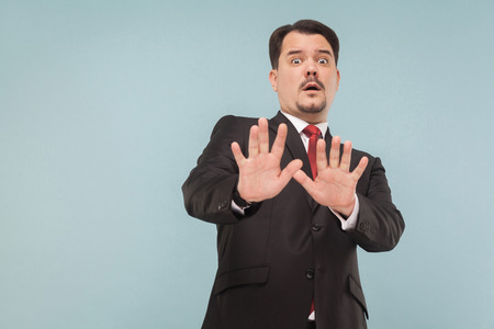Businessman panic. Nervous man in suit scared and looking at camera with fear in eyes. indoor studio shot. isolated on light blue background. handsome businessman with black suit, red tie and mustacheの写真素材