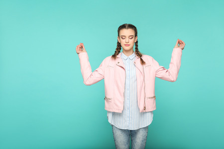 meditation and yoga portrait of beautiful cute girl standing with makeup and brown pigtail hairstyle in striped light blue shirt pink jacket. indoor, studio shot isolated on blue or green background.の写真素材