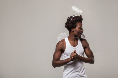 thoughtful confused man. dark skinned angel with nimbus and winks standing with raised arm and profile side thinking and looking. studio shot, Indoor, isolated on gray backgroundの写真素材