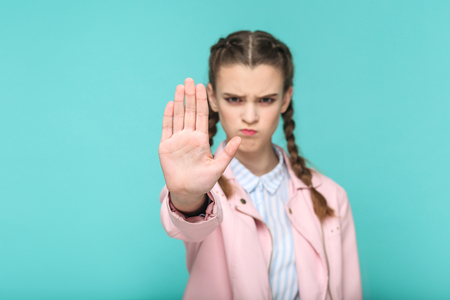 stop it, serious portrait of beautiful cute girl standing with makeup and brown pigtail hairstyle in striped light blue shirt pink jacket. indoor, studio shot isolated on blue or green background.の写真素材