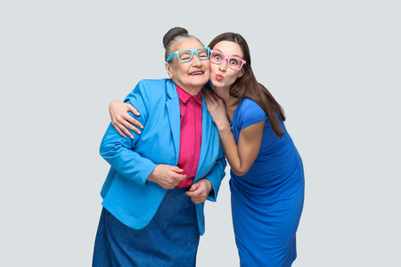 Grandmother with grandchild hugging and have fun together in family. kiss and toothy smile and good relationship. Friendship and mutual understanding. indoor, studio shot, isolated on gray backgroundの写真素材