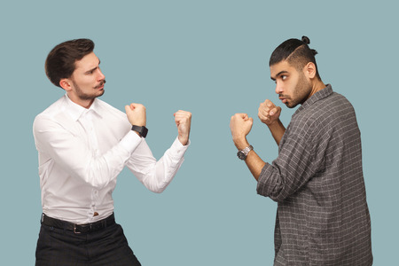 profile side view of two angry boxer businessman, looking to each other with serious face and ready to attack. crisis and partnerships problem. indoor studio shot, isolated on light blue background.の写真素材