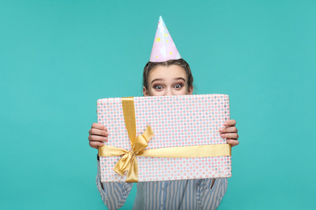 surprised girl in striped blue shirt standing and holding in front of face dotted gift box and...