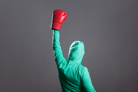 Back side view of winner muslim boxer woman in green islamic sports wear, standing in red boxing gloves and celebrating her victory, hands up. indoor studio shot, isolated on dark grey backgroundの写真素材