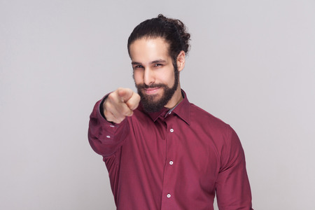 Hey you. Portrait of handsome man with dark collected long hair and beard in red shirt standing,...