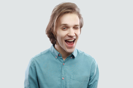 Portrait of funny happy handsome long haired blonde young man in blue casual shirt standing and...