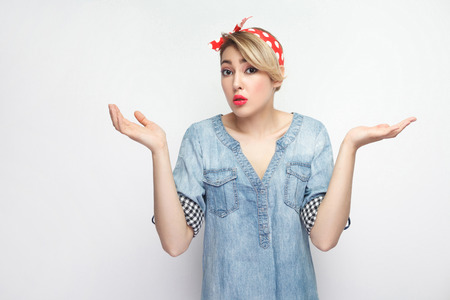 I don't know. Portrait of confused beautiful young woman in casual blue denim shirt with makeup and red headband standing, looking and dont know what to do. studio shot, isolated on white background.の写真素材