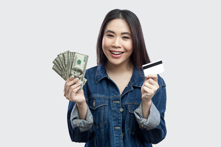 Portrait of beautiful happy young asian girl in blue denim jacket standing and holding bank credit...