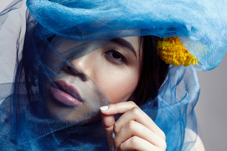 portrait of sensual gorgeous asian woman looking at camera through blue veil on face . indoor studio shot.の写真素材
