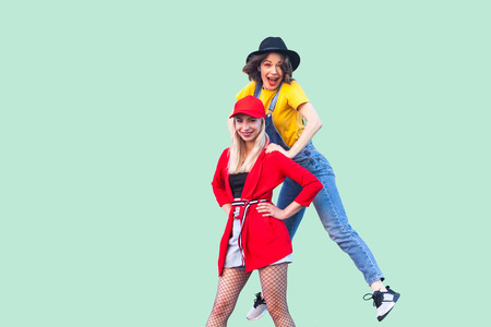 Portrait of two best friend beautiful amazing happy fashionable hipster girls, one girl jumping up...