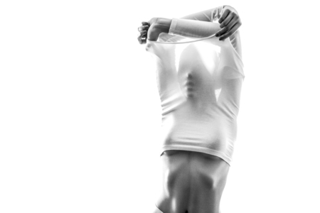 Portrait of young woman in white t-shirt standing, undressing white shirt with passion and covering or hiding face. black and white photography, indoor studio shot, isolated on white background.の写真素材