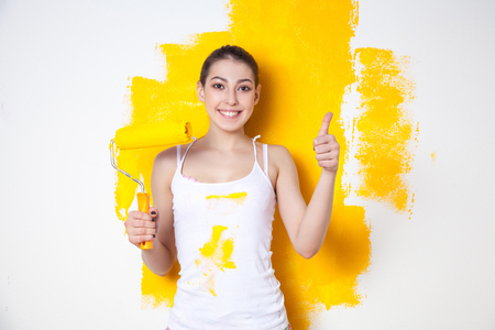 Beautiful young caucasian model in coloured shorts and white shirt and posing holding outrigger in her hands, painting the wall and looking at camera. Studio shot.の写真素材