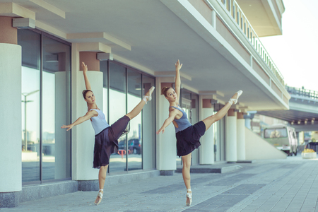 Two young beautiful twin sister dancing ballet in the city with ballet costume. urban sync dance. industrial street dancing. with special effect. synced posing. pointe ballet shoes and dress.の写真素材