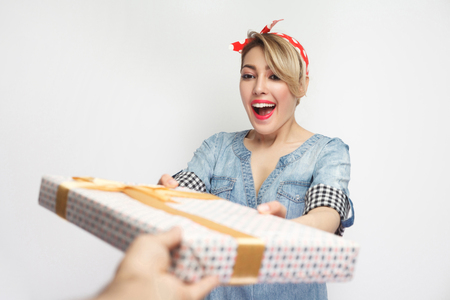 Portrait of beautiful young woman in casual blue denim shirt with makeup and red headband standing, receiving gift with happy toothy smiling face. indoor studio shot, isolated on white background.の写真素材