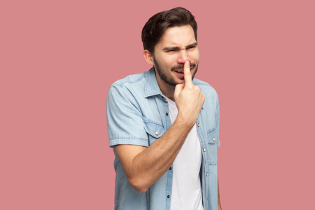 You are liar. Portrait of angry handsome bearded young man in blue casual style shirt standing, touching his nose and showing lie gesture. indoor studio shot, isolated on pink background.の写真素材