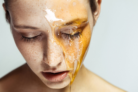 Portrait of beautiful young brunette woman with freckles and honey on face with closed eyes and serious face, head down. indoor studio shot isolated on gray background.の写真素材