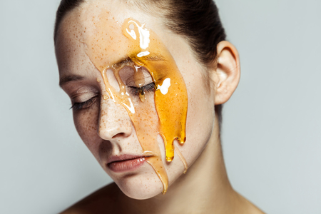Portrait of beautiful young brunette woman with freckles and honey on face with closed eyes and serious face. indoor studio shot isolated on gray background.の写真素材