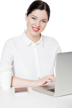 Portrait of happy successful attractive brunette businesswoman in white shirt sitting with laptop, looking with toothy smile satisfied face expression. indoor studio shot, isolated in white backgroundの写真素材
