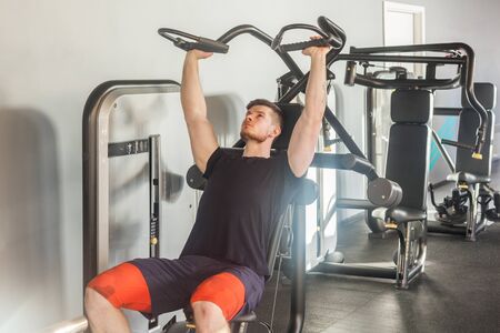Portrait of young adult sport athlete man training at gym alone and lifting weights while sitting on...