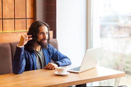 Please little bit! Portrait of cunning young adult man freelancer in casual style sitting in cafe with laptop, looking at camera, showing with finger to make less loud music. Indoor, lifestyle conceptの写真素材