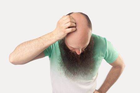 Portrait of middle aged bald man with long beard in light green t-shirt standing and showing his baldness on his head. indoor studio shot, isolated on grey background.の写真素材