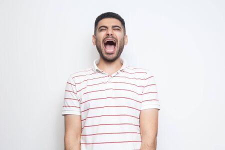 Portrait of funny handsome bearded young man in striped t-shirt standing with closed eyes and laughing. indoor studio shot, isolated on white background.の写真素材