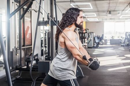 Side view of young adult confident crossfit man with long curly hair standing and doing trx...