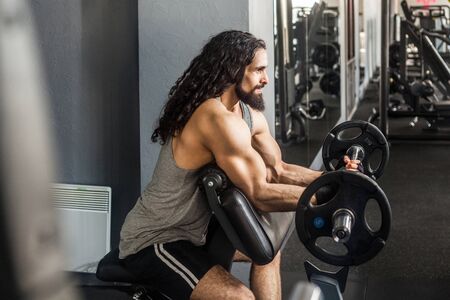 Side view portrait of young adult bodybuilder with long curly hair are workout in gym alone and...