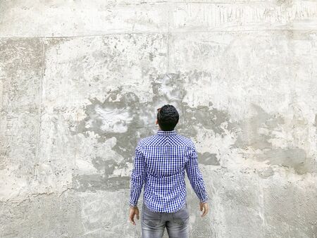 Backside of young man in checkered blue shirt and sunglasses standing against concrete gray wall. looking at background empty copyspace.の写真素材