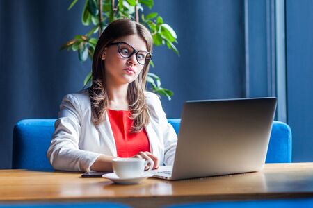 Portrait of crazy beautiful stylish brunette young woman in glasses sitting and looking at laptop...