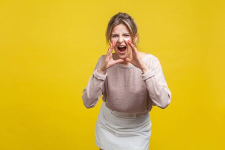Portrait of aggressive young woman with fair hair in casual blouse standing with hands near mouth...