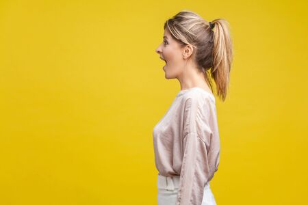 Profile side view of happy amazed blonde woman with ponytale hairstyle and in casual beige blouse...