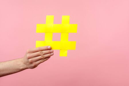 Closeup of male hand holding large yellow hashtag sign, concept of marketing and promotion in internet, followers in social media, trend content. indoor studio shot isolated on pink backgroundの写真素材