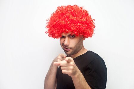 Hey you, beauty! Portrait of funny positive man with bristle and red wig pointing to camera and winking playfully, flirting and getting acquaintance, asking for a date. studio shot, white backgroundの写真素材