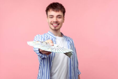 Portrait of successful rich brunette man with small beard and mustache in casual shirt proposing dollars to camera, giving big sun of money, investment. indoor studio shot isolated on pink backgroundの写真素材