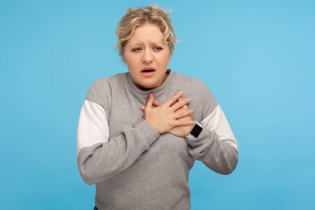 Heart attack. Portrait of tired overworked woman with short curly hair in sweatshirt clutching...