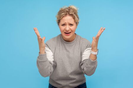 How could you? Displeased woman with short hair in casual sweatshirt raising hands in questioning...
