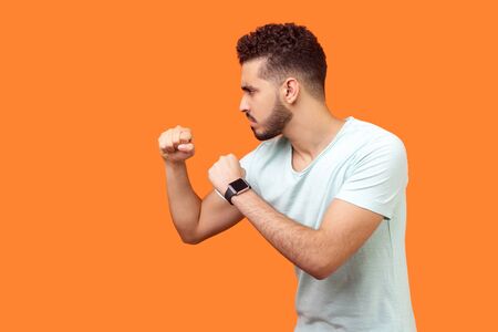 Boxing and self-defence. Side view of aggressive man with beard in white t-shirt keeping fists...