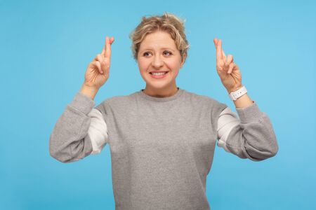Need fortune. Positive woman with short hair in sweatshirt holding crossed fingers and wishing for...