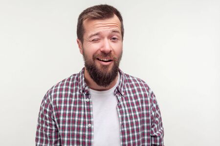 Portrait of handsome bearded positive man in plaid shirt smiling and winking playfully at camera with optimistic cheerful expression, wrinkles on face. indoor studio shot isolated on white backgroundの写真素材